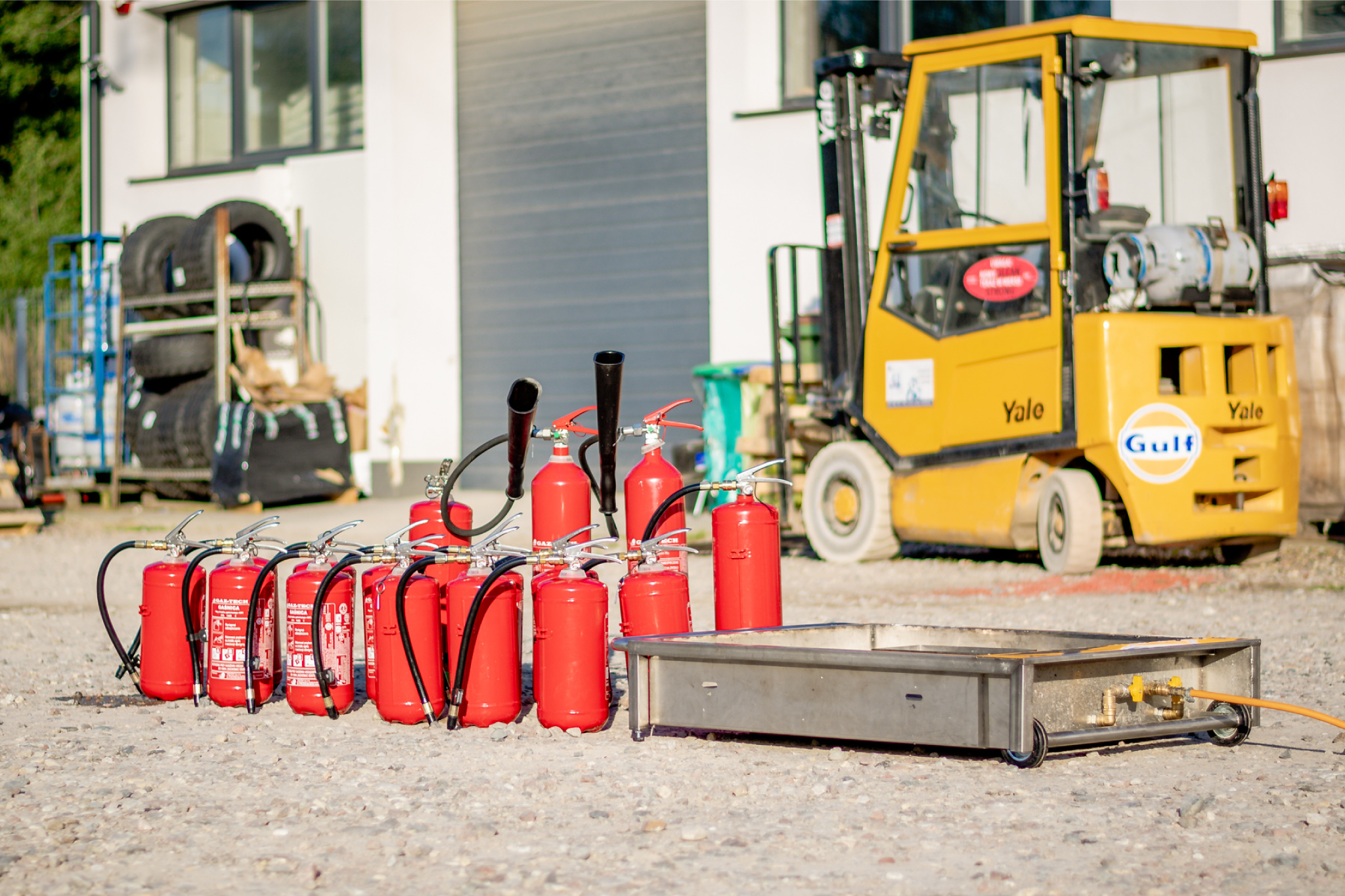 Zestaw gaśnic oraz trenażer ognia przygotowane do praktycznego szkolenia przeciwpożarowego na placu przemysłowym